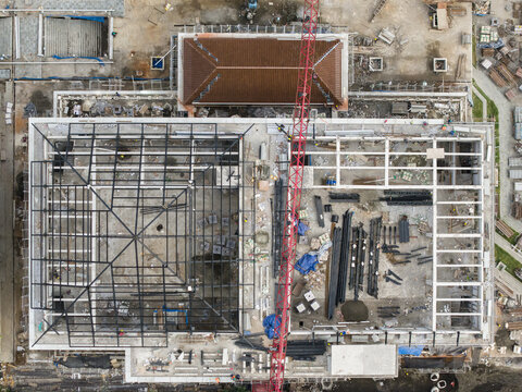 Aerial view of a building construction site featuring a steel frame structure, a tall red crane, and various building materials in Gianyar, Bali, Indonesia.