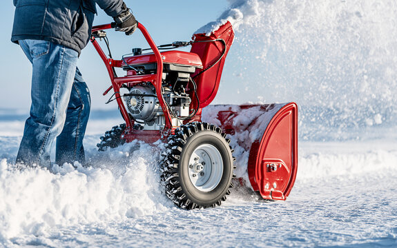 Person operating red snow blower to clear snow from driveway in winter