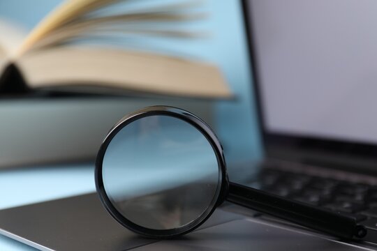 Keywords. Magnifying glass, laptop and books on light blue background, selective focus