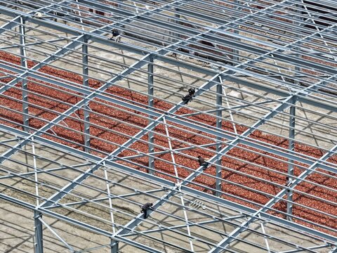 Aerial view of the Aminbazar 400230132 kV Grid Substation construction site with workers installing steel beams over red gravel in Aminbazar, Dhaka Division, Bangladesh.