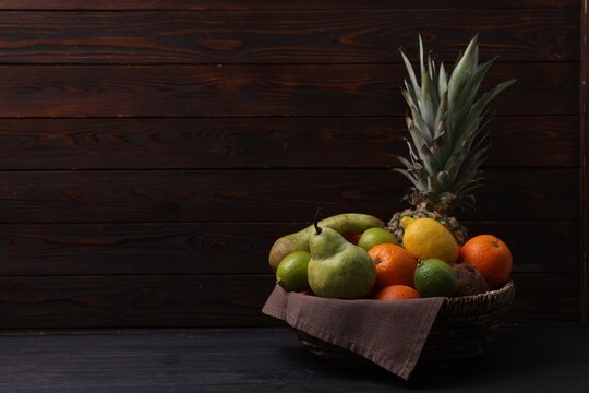 Different fresh fruits in wicker basket on black wooden table, space for text