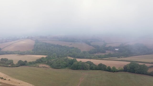 Aerial drone flight over misty agricultural fields in Looe, Cornwall on a foggy morning.