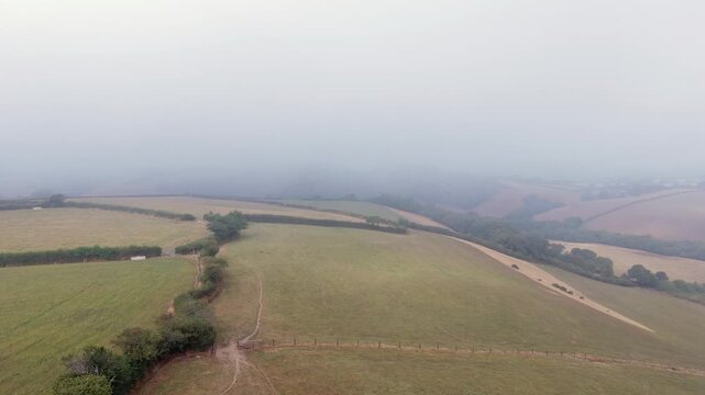 Aerial drone flight over foggy agricultural fields in Looe, Cornwall at sunrise