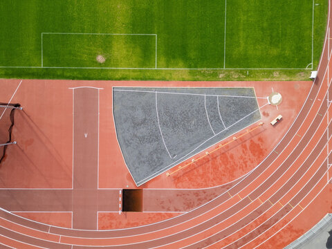 Aerial view of a sports arena featuring a red running track, a green grass field, and a grey shot put area in Oulu, North Ostrobothnia, Finland.