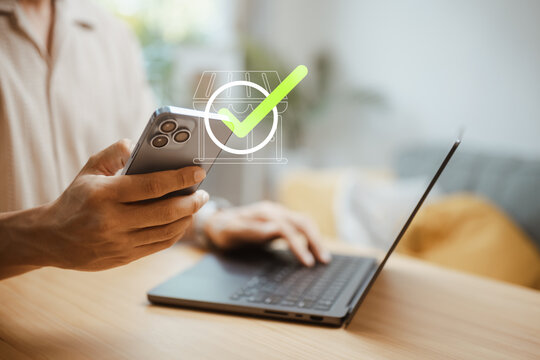 A smartphone user receives a green confirmation check beside a laptop after an order is confirmed and the item details are saved for customer reference and delivery tracking before shipment begins.