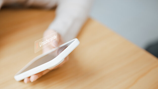 A hand taps an Unsubscribe command on a smartphone to cancel a subscription and prevent its automatic renewal before another charge reaches the linked payment card during the next month.