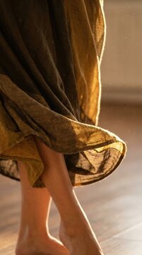 Barefoot dancer's legs in flowing fabric, showcasing movement and texture against a warm wooden floor in a softly lit indoor space