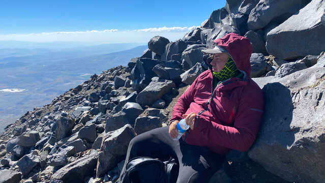 Climber hydrating while resting in medium shot on the rocky slope of Mount Ararat, Turkey, showing water intake