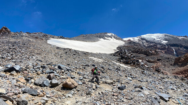 Hiker descends Mount Ararat, wide view across steep volcanic rocks and lingering snow in eastern Turkey