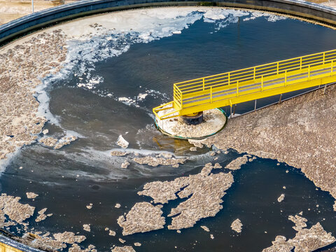 Aerial view of a circular clarifier at a wastewater treatment plant with a yellow metal walkway, showing industrial water processing in Florianopolis, Santa Catarina, Brazil.