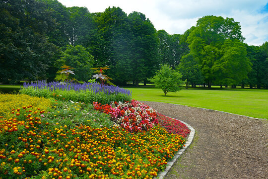 Beautiful Landscaped Park Garden With Bright Red Yellow Purple Flowers Blooming Next To Curved Walkway Path.