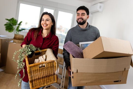 Smiling couple carrying moving boxes and a wicker basket inside their home