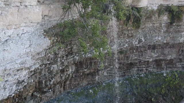 A small, serene waterfall cascades from rocks in a nature video in the forest.