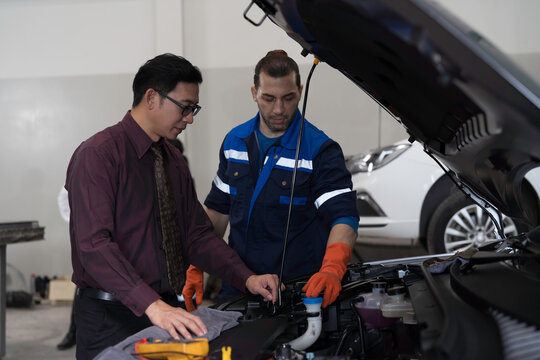 Mechanic and customer inspects and repairs car engine and components with hood open inside services garage
