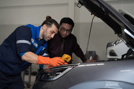 Mechanic and customer inspects and repairs car engine and components with hood open inside services garage