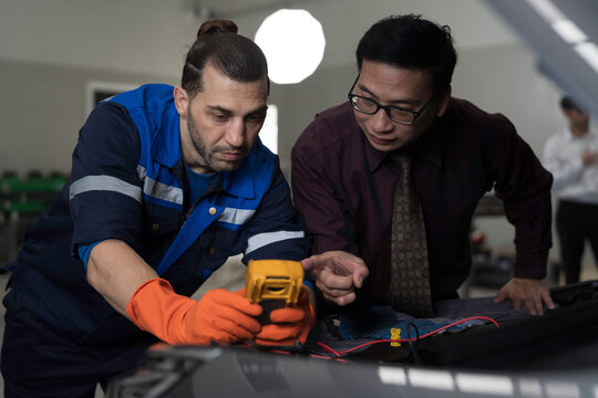 Mechanic and customer inspects and repairs car engine and components with hood open inside services garage