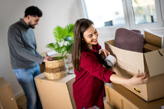 Couple carrying cardboard boxes and a plant while moving home