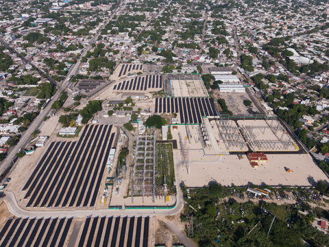 Aerial view of CFE Merida Area solar farm and electrical substation with rows of solar panels, power transformers, and surrounding urban infrastructure in Merida, Yucatan, Mexico.