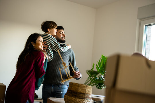 Family carrying young son while moving belongings into a new home