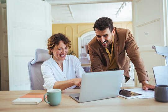 Smiling Colleagues Collaborating Over Laptop in Modern Office During Casual Business Meeting