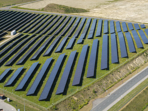 Aerial view of solar panels arranged in rows across a grassy field near a road in Poland.