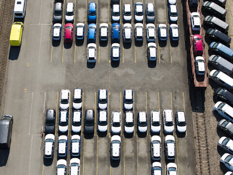 Aerial view of a car logistics terminal with rows of new vehicles parked in a lot and loaded onto a train carriage in Poland.