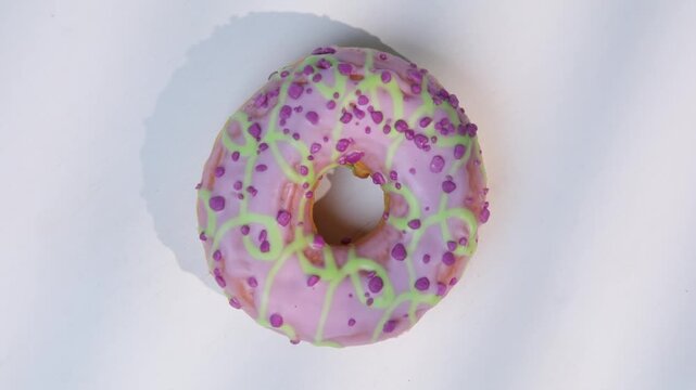 Sweet donut with pink icing and sprinkles on a white surface, top view, donut spinning