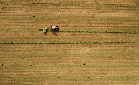 Aerial view of a tractor harvesting hay in a large agricultural field with scattered hay bales in Greece.