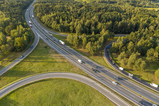 Aerial view of highway interchange with vehicles driving on multi-lane roads surrounded by lush green forest and grassy fields in Krakow, Lesser Poland Voivode, Poland.