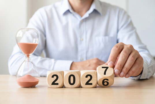 Man changing wooden number blocks from 2026 to 2027 beside an hourglass as a concept of new year transition, countdown, future planning and passage of time.