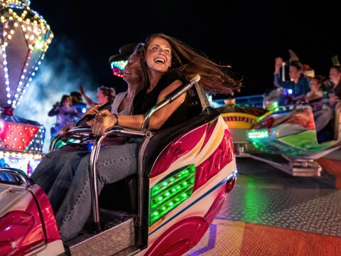 Hoher Freifallturm auf einem deutschen Volksfest bei farbenpr&auml;chtigem Sonnenuntergang. Besucher, Fahrgesch&auml;fte und leuchtende Kirmes schaffen eine lebendige Jahrmarktatmosph&auml;re.