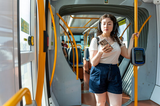Young woman with vitiligo enjoying music, commuting on a modern urban tram