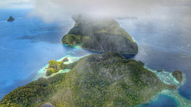 Aerial view of the lush green islands and turquoise coral reefs of Raja Ampat Regency in Southwest Papua, Indonesia.