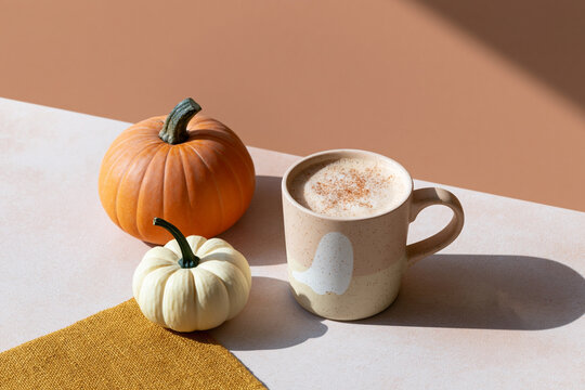 Halloween coffee with creamy foam in ghost mug beside orange and white pumpkins, cozy autumn still life in warm sunlight with copy space