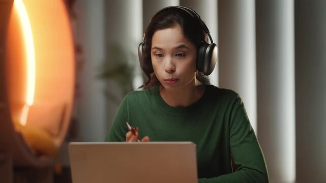 Young Asian woman in headset conducts video lesson on laptop, e-learning