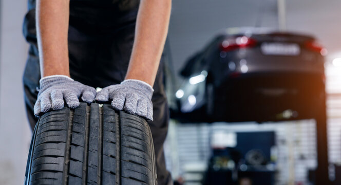 Car wheel service: mechanic in blue overalls working on tire replacement in garage.