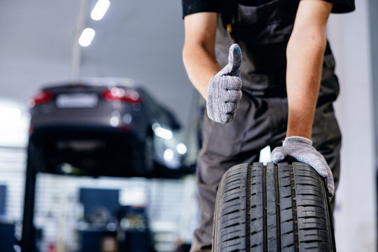 Mechanic showing thumbs up with tire in automotive workshop, service for change of wheels