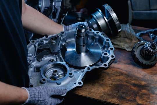 Worker inspecting gearbox housing on wooden workbench in repair shop, fix service concept