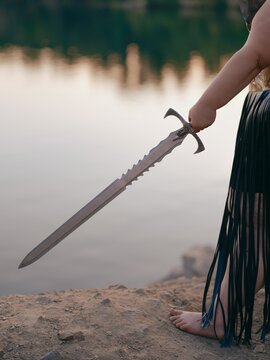 Woman Hand Holding Fantasy Sword near Lake Close-Up Outdoor