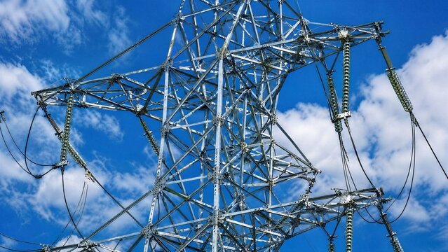 High-Voltage Transmission Tower Under Blue Sky: A towering electrical pylon stands against a bright blue sky with fluffy white clouds, conveying power and industrial strength.