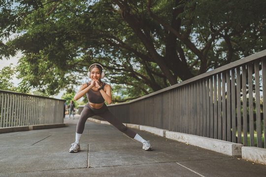 Happy sporty woman wearing headphones doing side lunge stretch outdoors, fitness training and active lifestyle