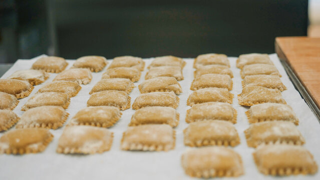 Handcrafting traditional Italian tortelli pasta squares, dusted with flour and arranged on a tray, showcasing the authentic culinary heritage of Bologna, Emilia Romagna region