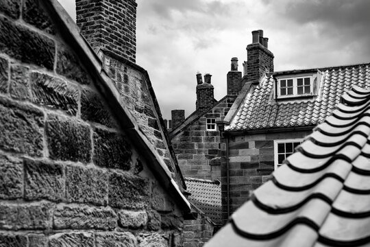 Black and white view of historic stone cottages, tiled rooftops and brick chimneys in the old fishing village of Robin Hood&rsquo;s Bay, North Yorkshire, England.