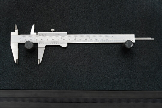 Precision stainless steel vernier caliper with metric and imperial measurement scales on a black surface for accurate dimensional measurement