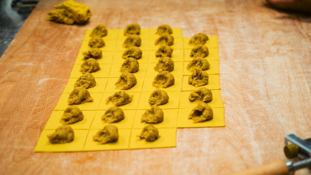 Rows of fresh pasta squares are topped with filling, ready to be folded into tortelli, a traditional Italian delicacy