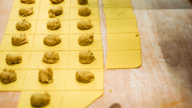Preparing traditional tortelli pasta with filling on a wooden board, showcasing an authentic Italian recipe from Emilia Romagna, Bologna, making fresh handmade food