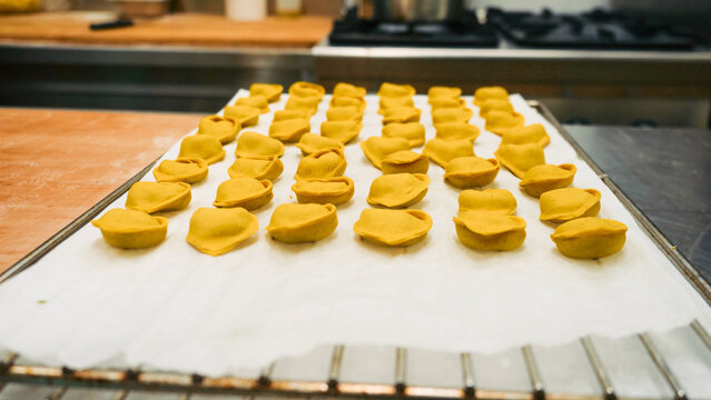 Artisanal tortelli pasta resting on baking paper, showing the detailed process of creating traditional Italian culinary delights in a kitchen in Bologna, Emilia Romagna