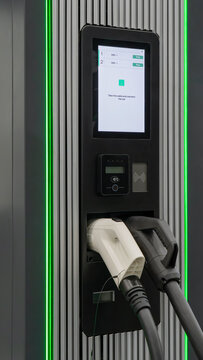 Close-up of an EV charger with screen instructions, contactless payment panel, and dual charging plugs with green LED lights.