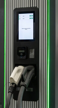 Modern electric vehicle charging station with digital display, payment terminal, and two connector cables for eco-friendly transportation