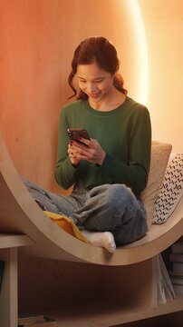 Young Asian woman texts on phone in modern library, sending video message